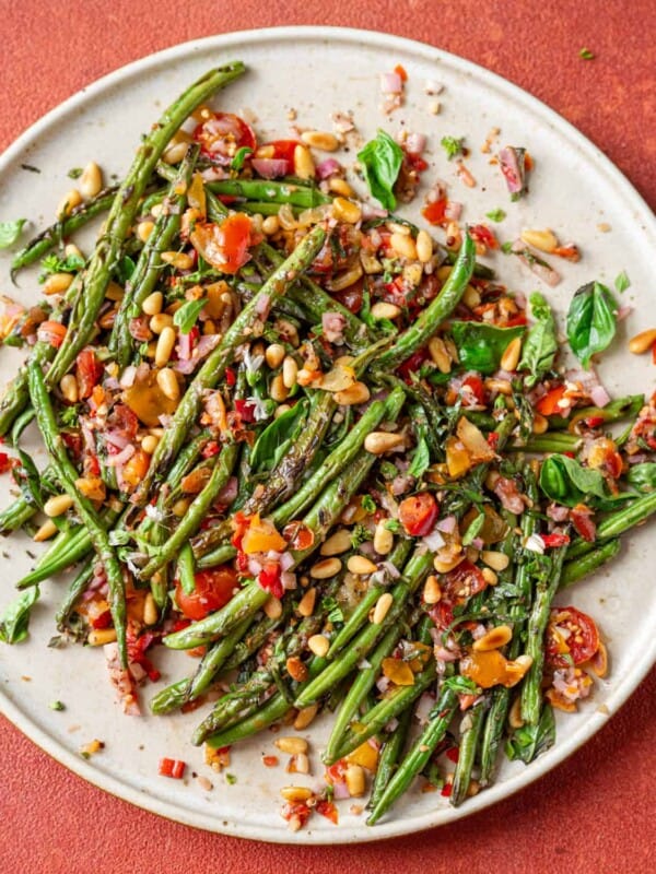 Overhead view of plate of charred green beans on a red table.