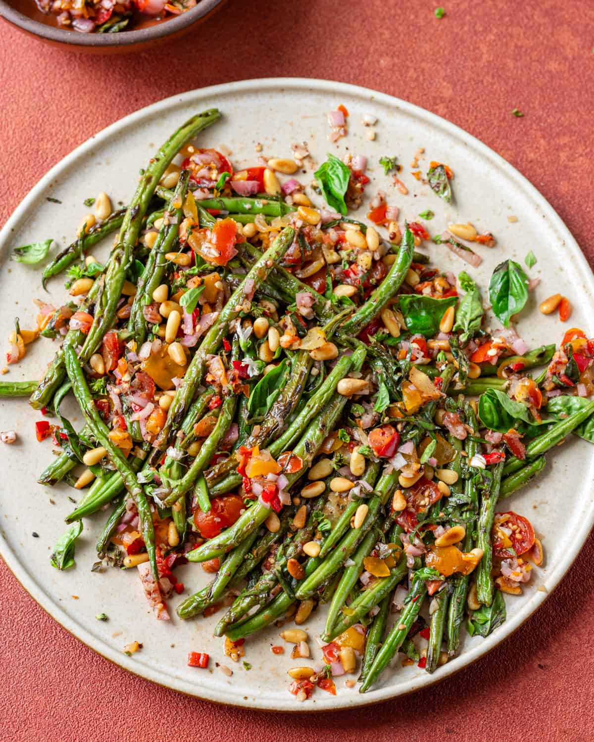 Overhead view of plate of charred green beans on a red table.