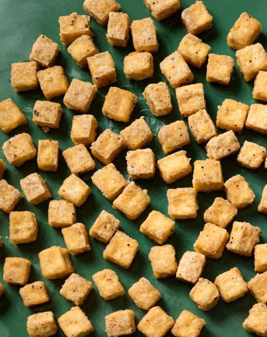 crispy baked tofu cubes on a green sheet pan.
