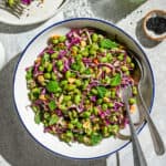 Bowl of edamame salad with two spoons on a white table.