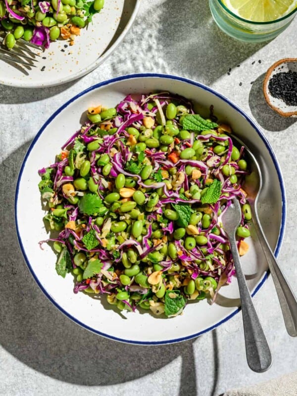 Bowl of edamame salad with two spoons on a white table.