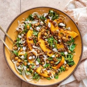 Pumpkin salad on a yellow plate next to a linen napkin on a tan table.