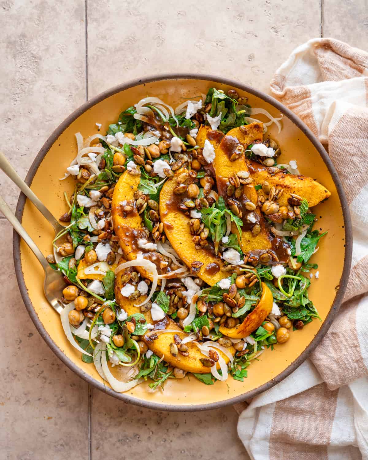 Pumpkin salad on a yellow plate next to a linen napkin on a tan table.