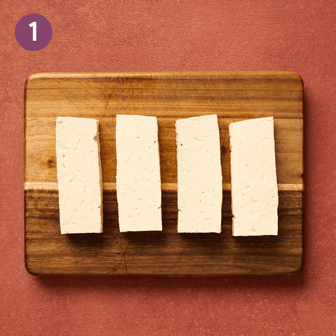 four tofu slabs on a wooden cutting board.