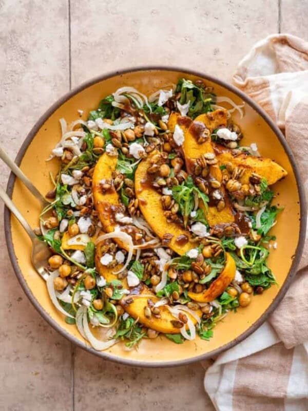 Pumpkin salad on a yellow plate next to a linen napkin on a tan table.