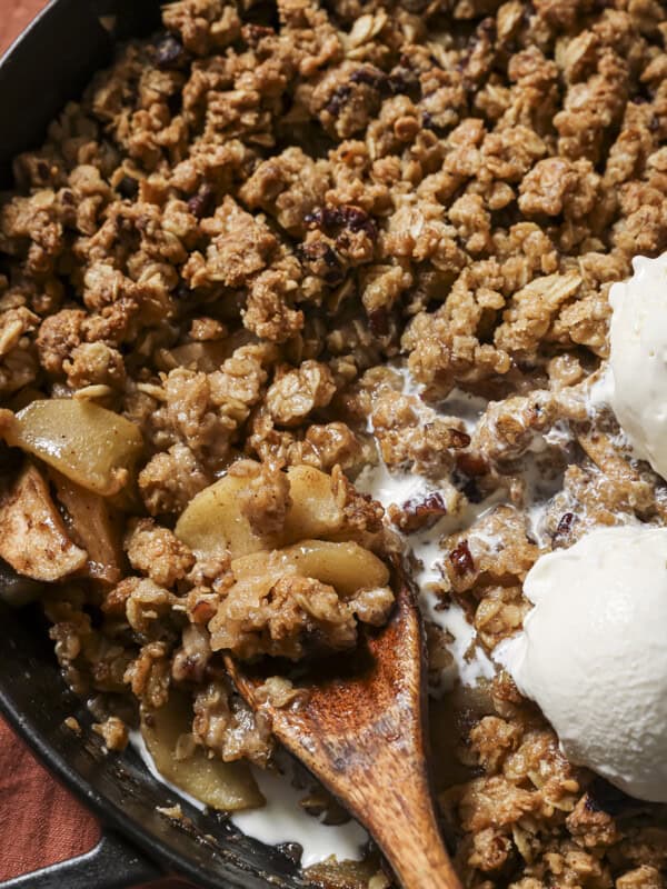 Apple crisp, vegan vanilla ice cream and a spoon in a cast-iron pan.