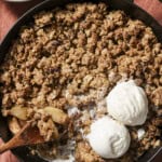 overhead view of skillet of apple crisp with two scoops of vanilla ice cream and a spoon.