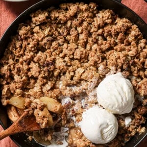 overhead view of skillet of apple crisp with two scoops of vanilla ice cream and a spoon.