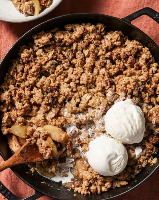 overhead view of skillet of apple crisp with two scoops of vanilla ice cream and a spoon.
