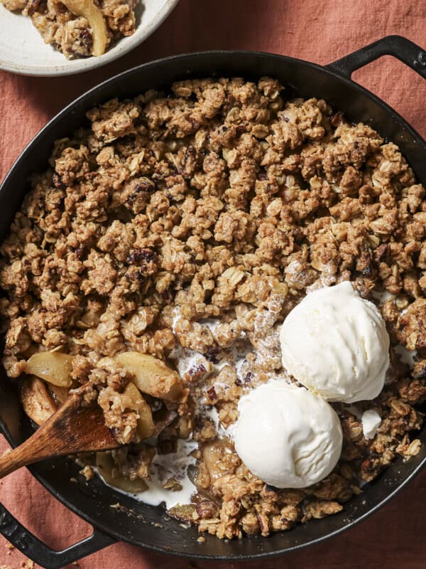 overhead view of skillet of apple crisp with two scoops of vanilla ice cream and a spoon.