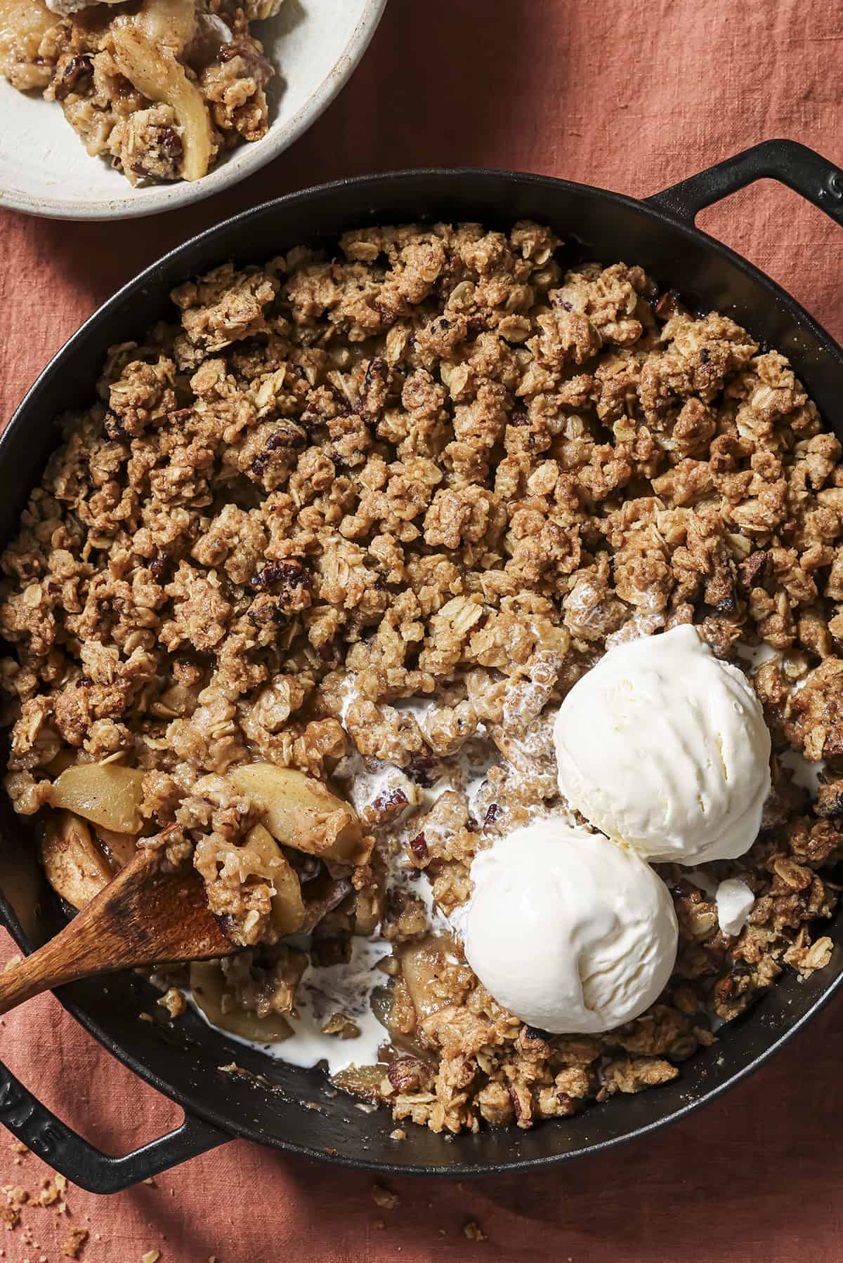 overhead view of skillet of apple crisp with two scoops of vanilla ice cream and a spoon.