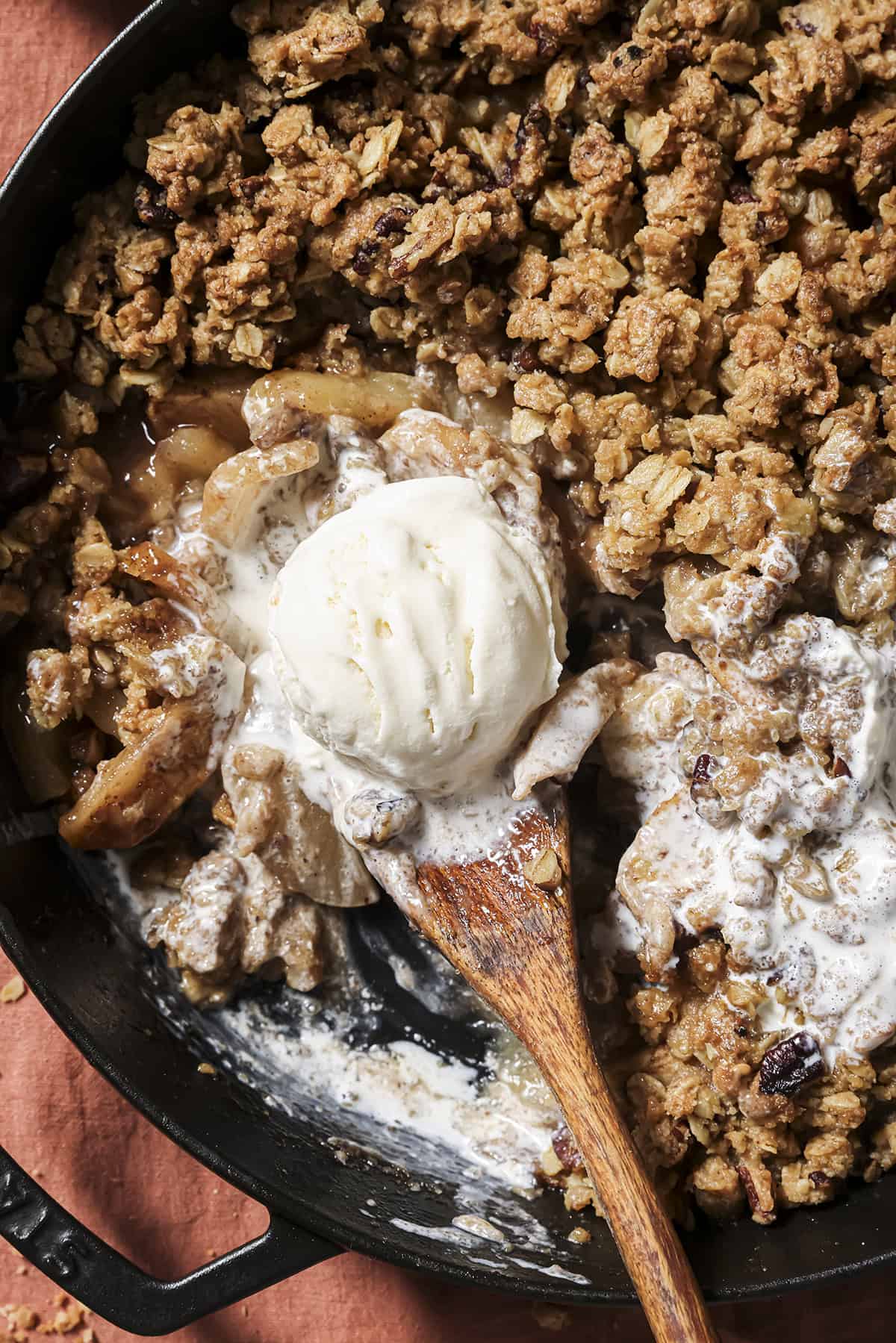 Overhead shot of someone using a large wooden spoon to lift a scoop of ice cream off the top of the apple crisp.