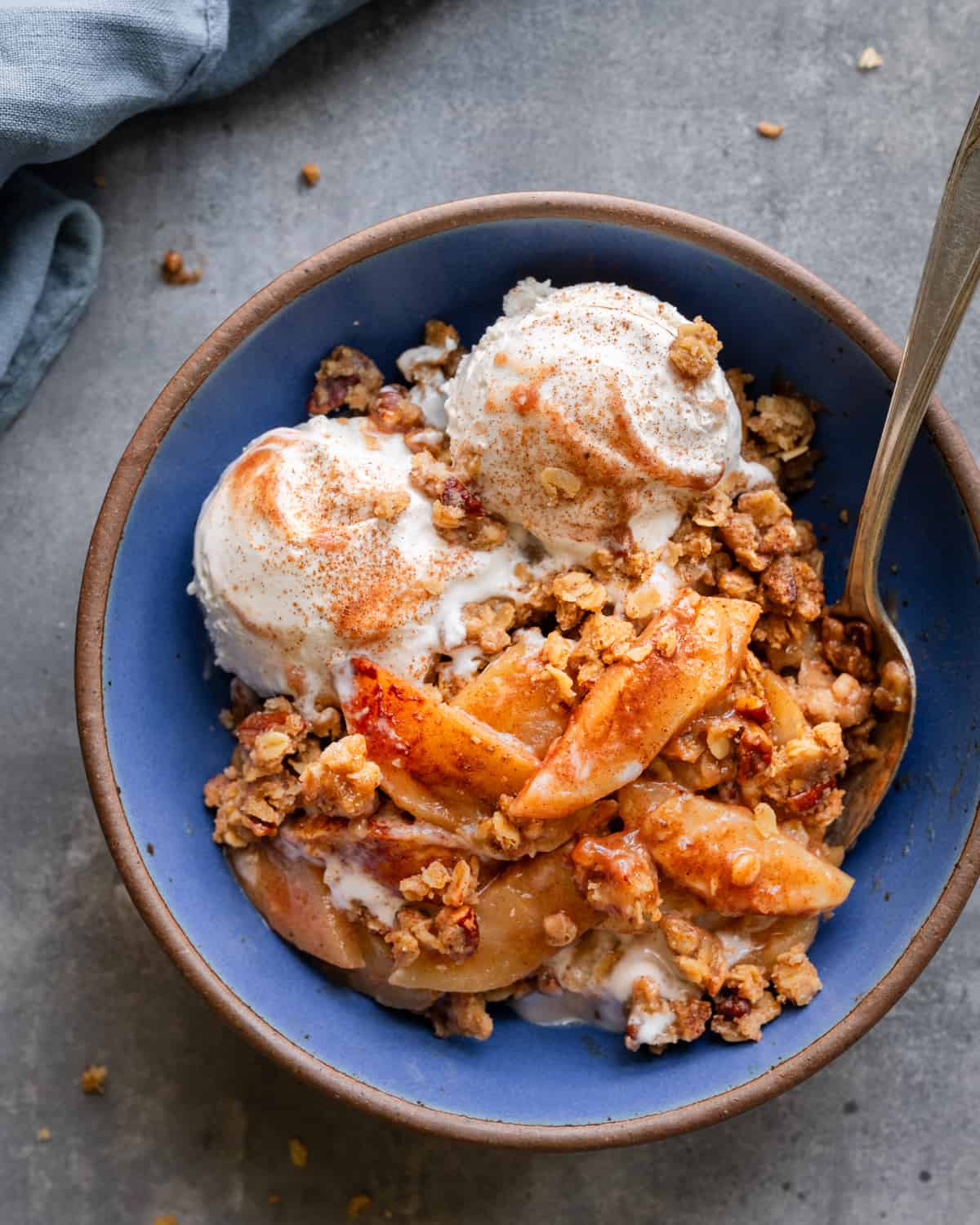 Apple crisp with vegan ice cream with a spoon in a blue bowl on a table.