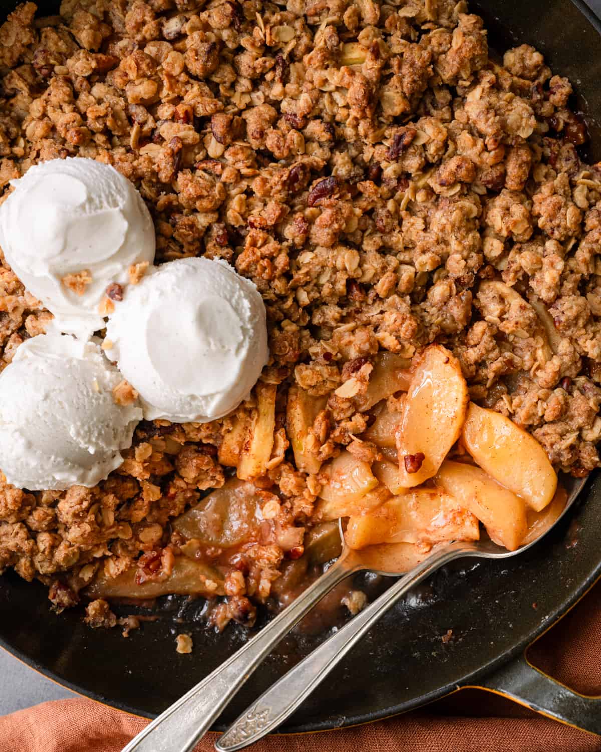 Two spoons in skillet of apple crisp with two scoops of ice cream.
