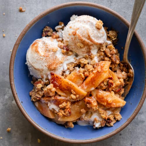 Apple crisp with vegan ice cream with a spoon in a blue bowl on a table.