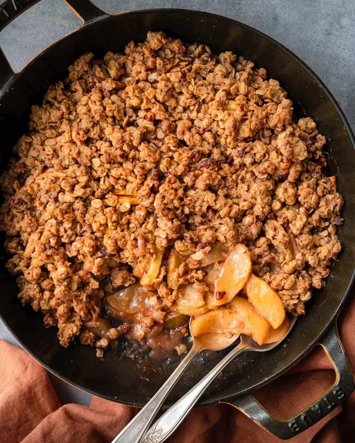 Two spoons in skillet of apple crisp on a table.