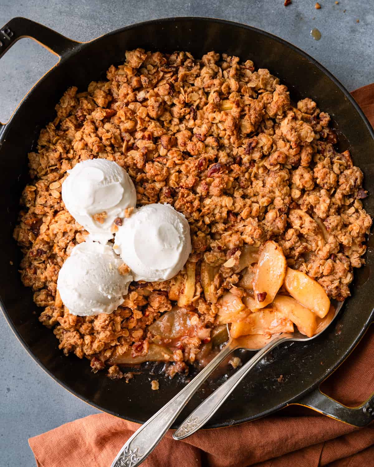 Two spoons in skillet of apple crisp with three scoops of ice cream.