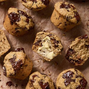 Overhead view of muffins on parchment paper, one is cut in half with butter on it.