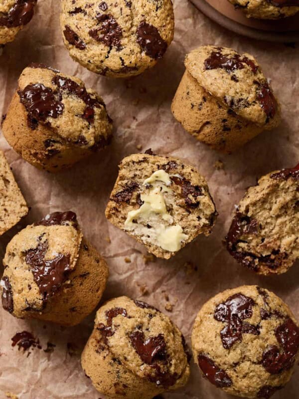 Overhead view of muffins on parchment paper, one is cut in half with butter on it.