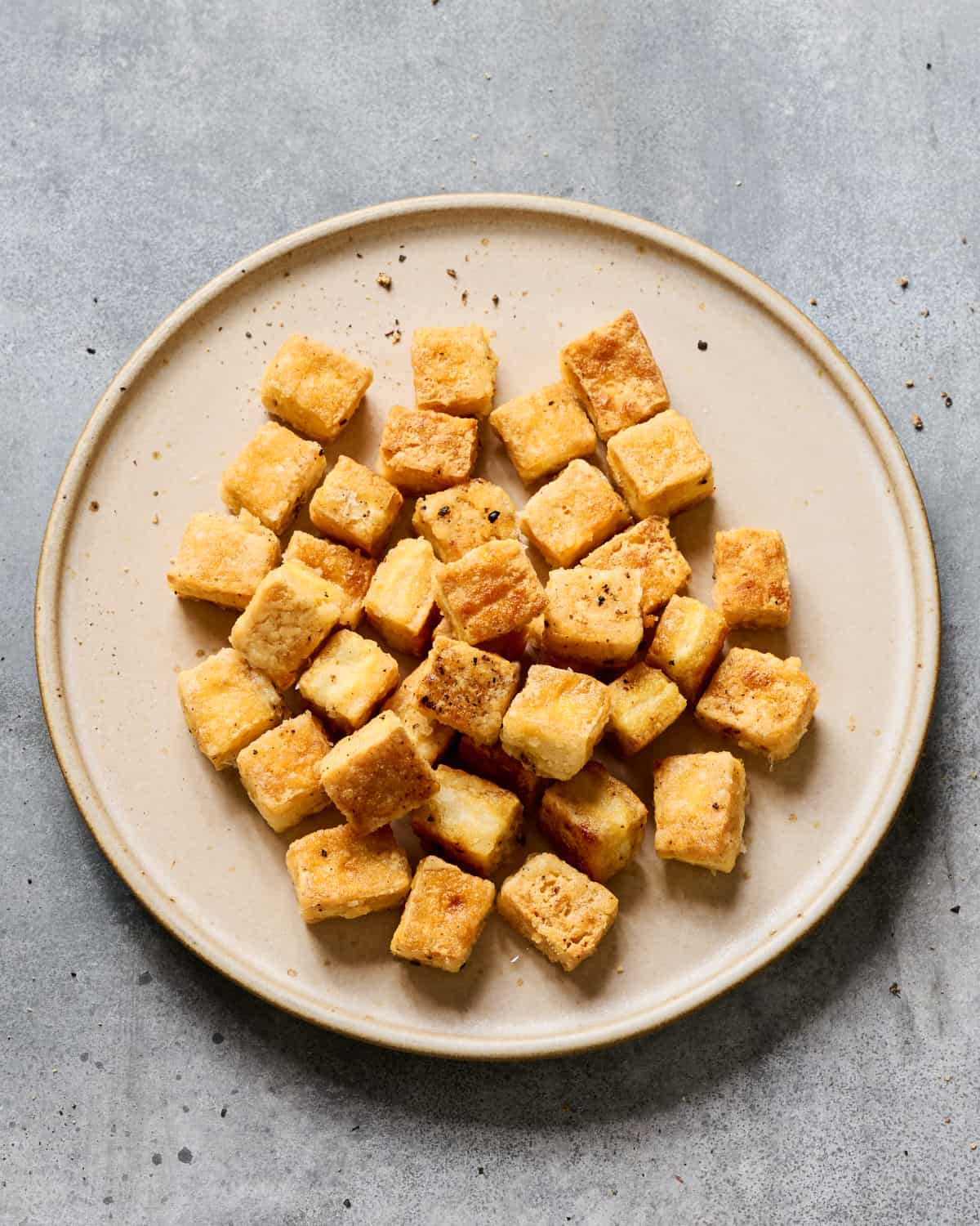 Fried tofu on a plate on a grey table.