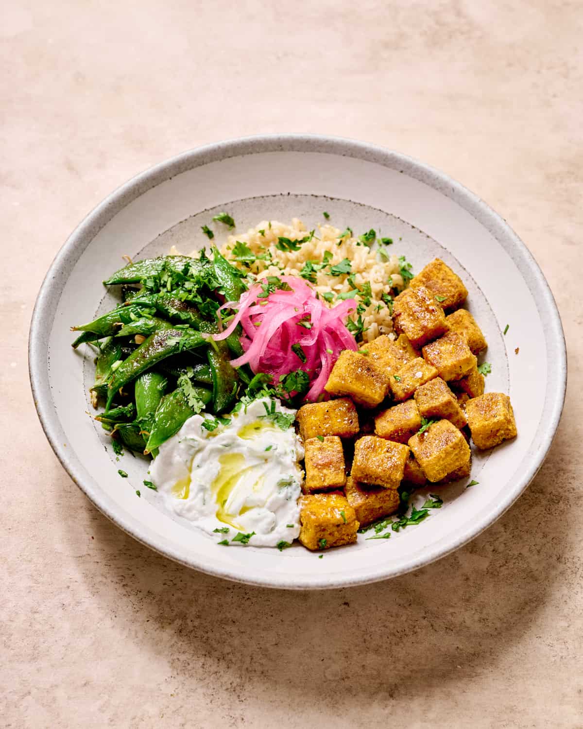 Indian spiced tofu in a bowl with rice, greens, vegan raita and pickled onions.