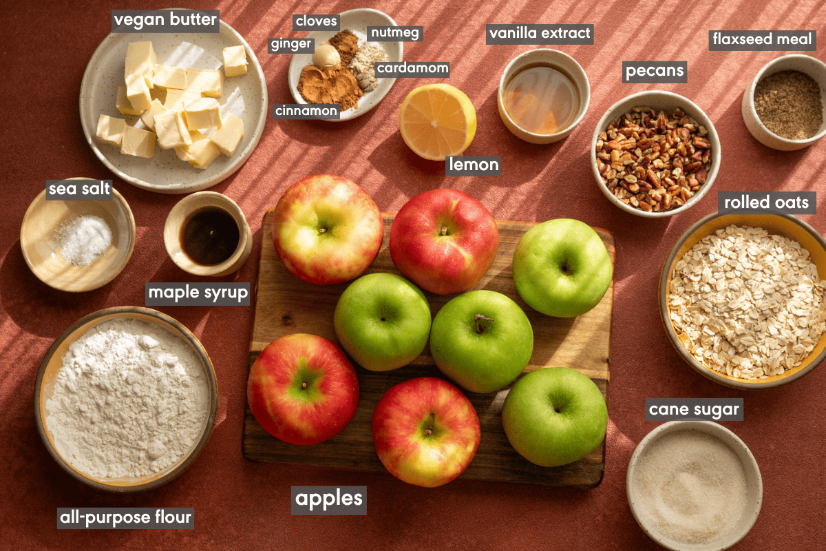 Vegan apple crisp ingredients in various small bowls on a red table.