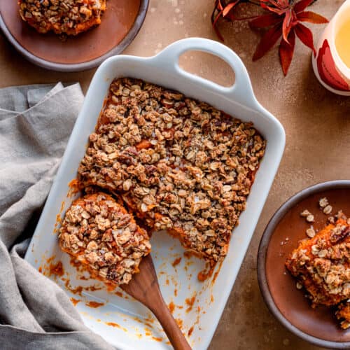 Overhead view of a wooden spoon in a sweet potato casserole on a brown table.