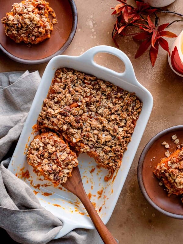 Overhead view of a wooden spoon in a sweet potato casserole on a brown table.