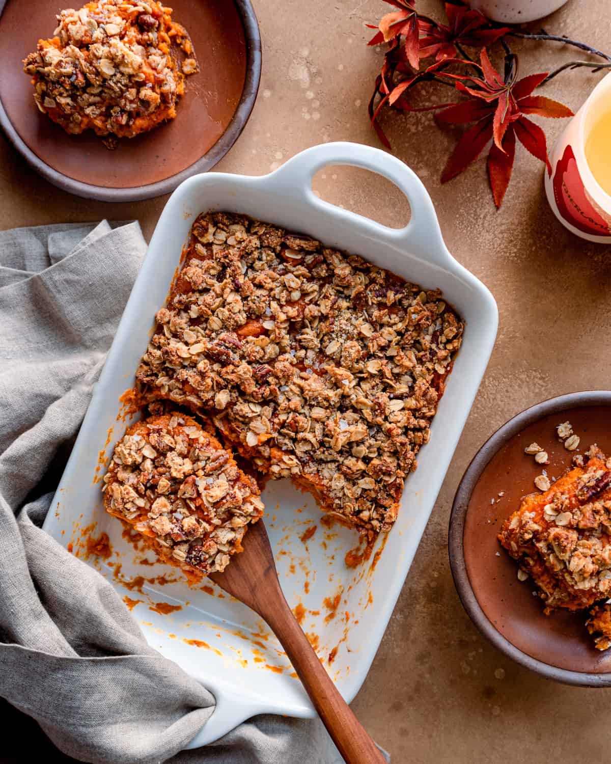 Overhead view of a wooden spoon in a sweet potato casserole on a brown table.