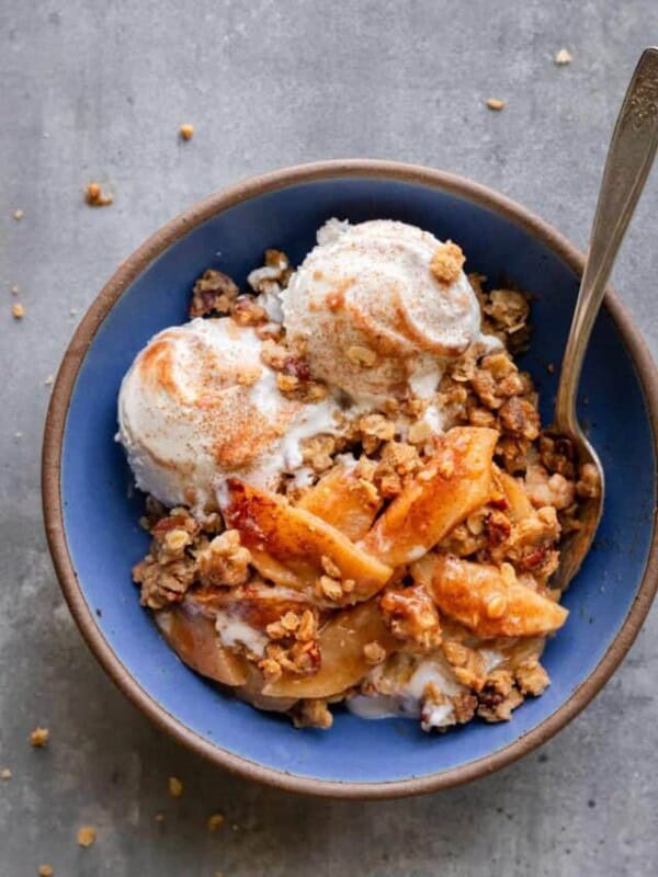 Apple crisp with vegan ice cream with a spoon in a blue bowl on a table.