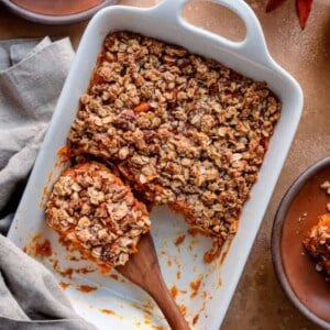 Overhead view of a wooden spoon in a sweet potato casserole on a brown table.