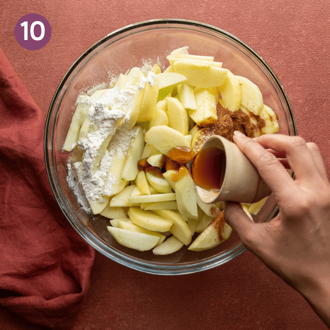 Person pouring maple syrup over apples with flour and spices in a bowl.