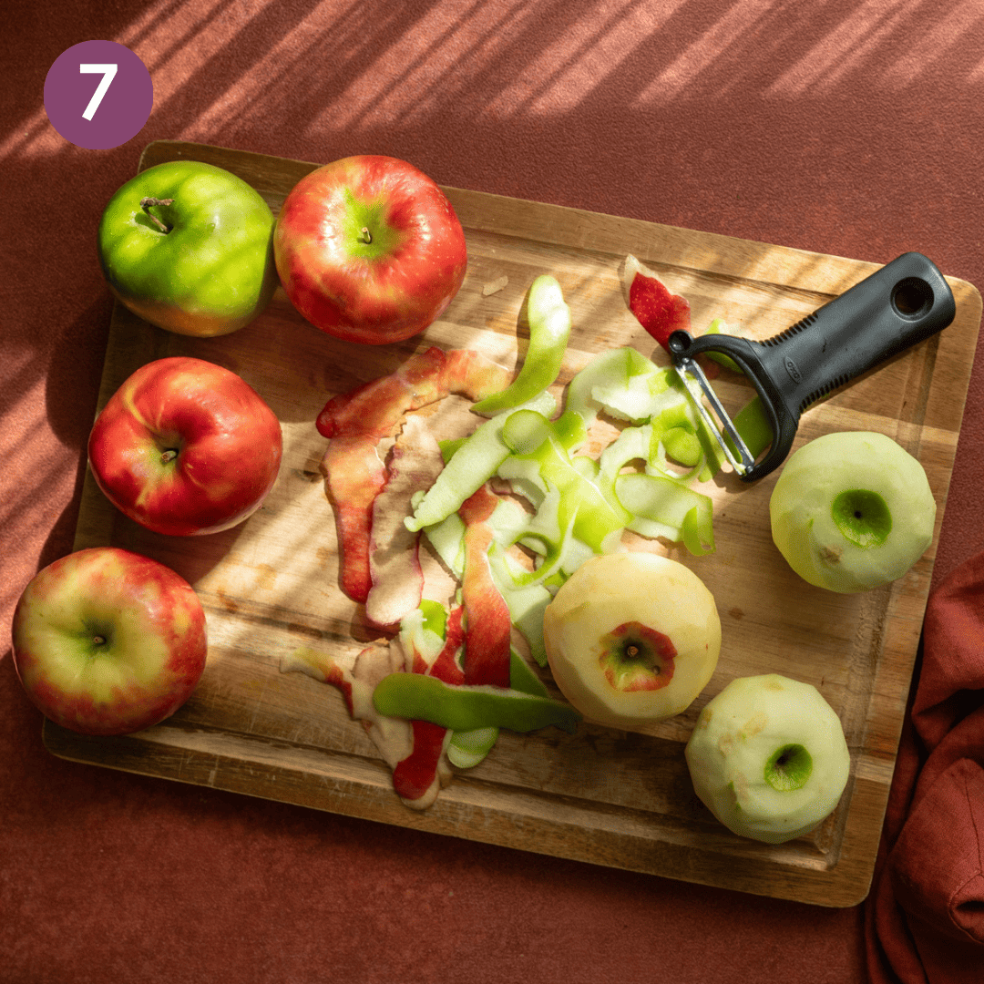 Peeled and unpeeled apples with y peeler on a wooden cutting board.