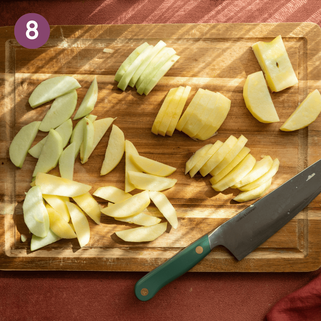 Sliced peeled apples and a knife on a wooden cutting board.