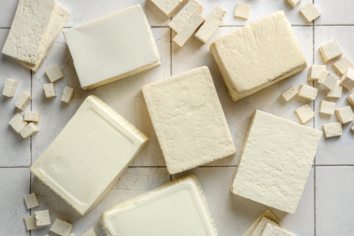 various types of tofu blocks and tofu cubes laid out on a tile table.
