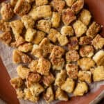 crispy torn pan fried tofu chunks on a piece of parchment paper on a red plate.