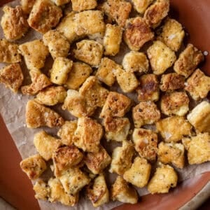 crispy torn pan fried tofu chunks on a piece of parchment paper on a red plate.