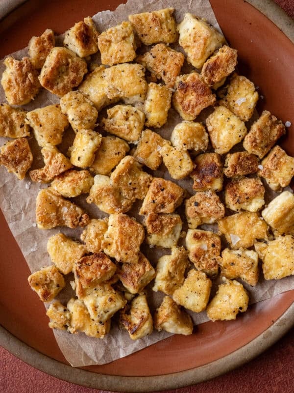 crispy torn pan fried tofu chunks on a piece of parchment paper on a red plate.