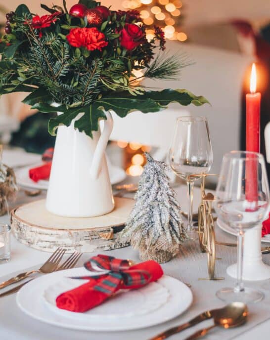 winter holiday table setup with flowers, candles, wine glasses and a tree in the background.