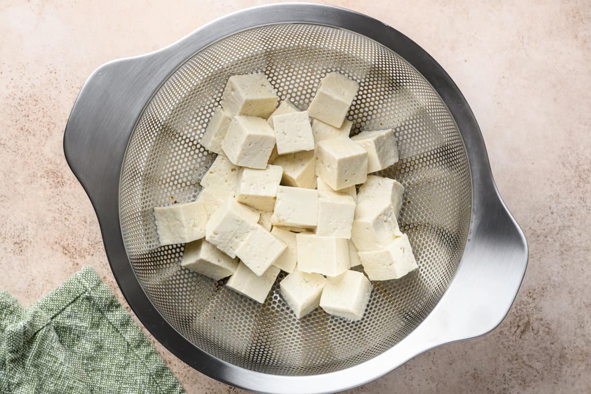 tofu cubes in a colander on a table.