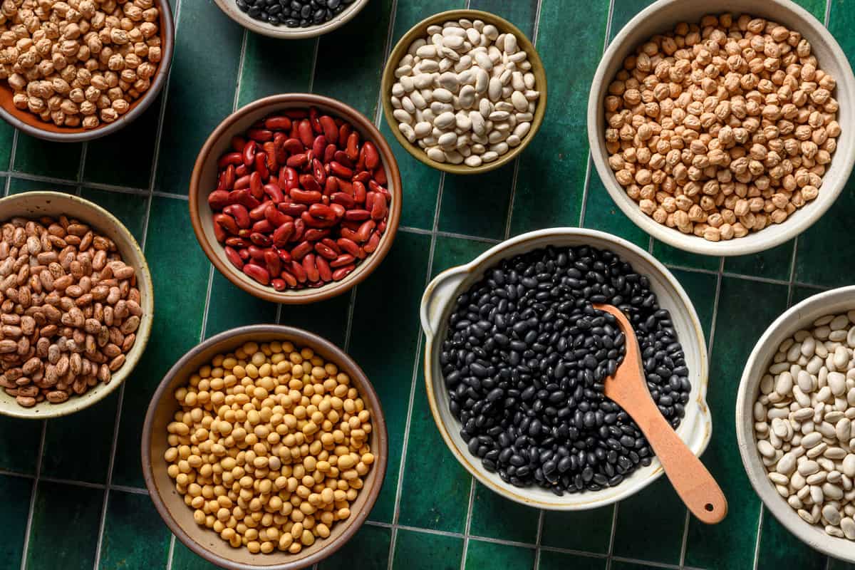 various types of beans in bowls on a table.