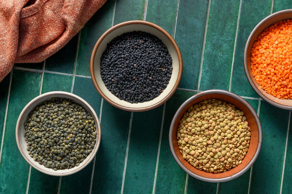 various types of lentils arranged in various bowls on a table.