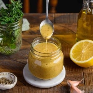 person taking a spoon from a glass jar of vinaigrette on a wooden table.