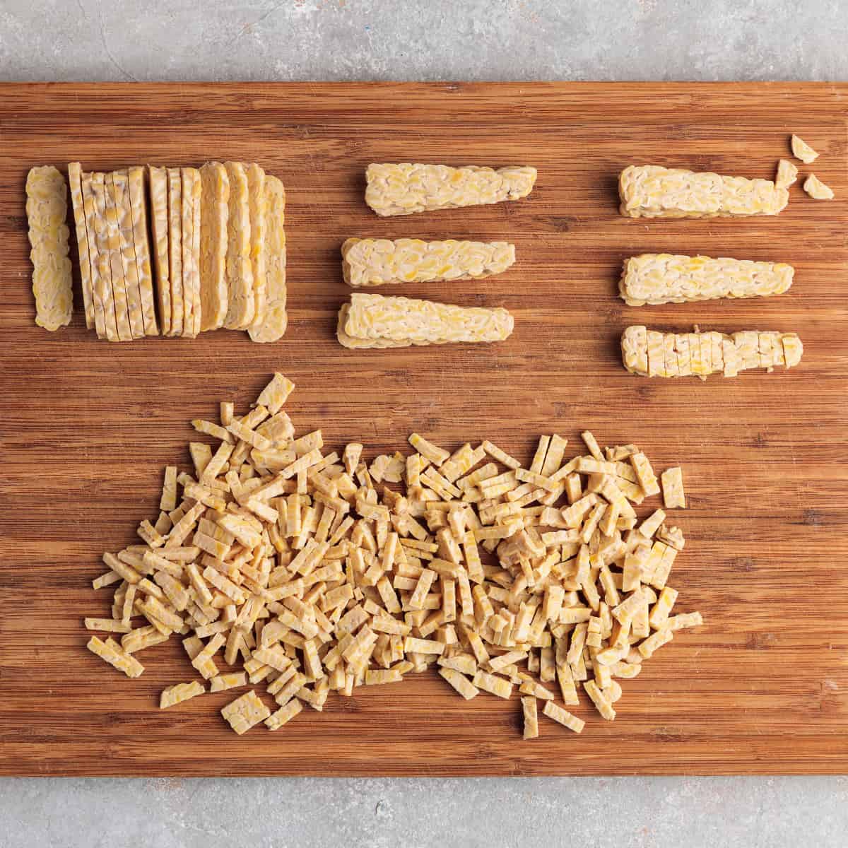 slices of tempeh on a wooden cutting board with some pieces cut into matchsticks. 