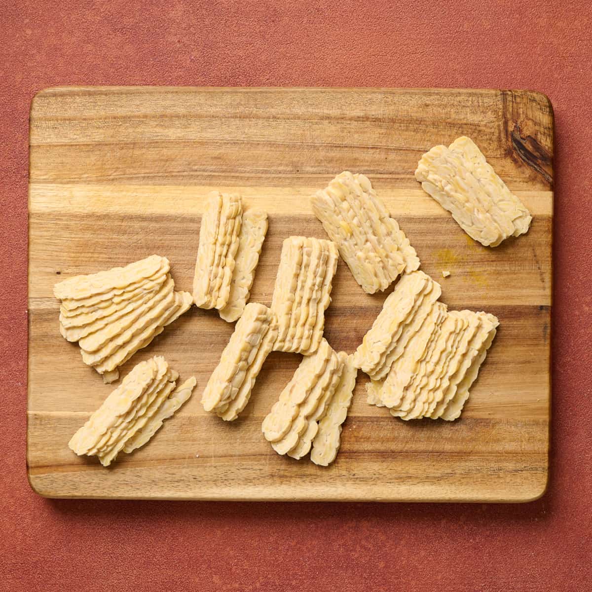 thinly sliced tempeh slices on wooden cutting board.