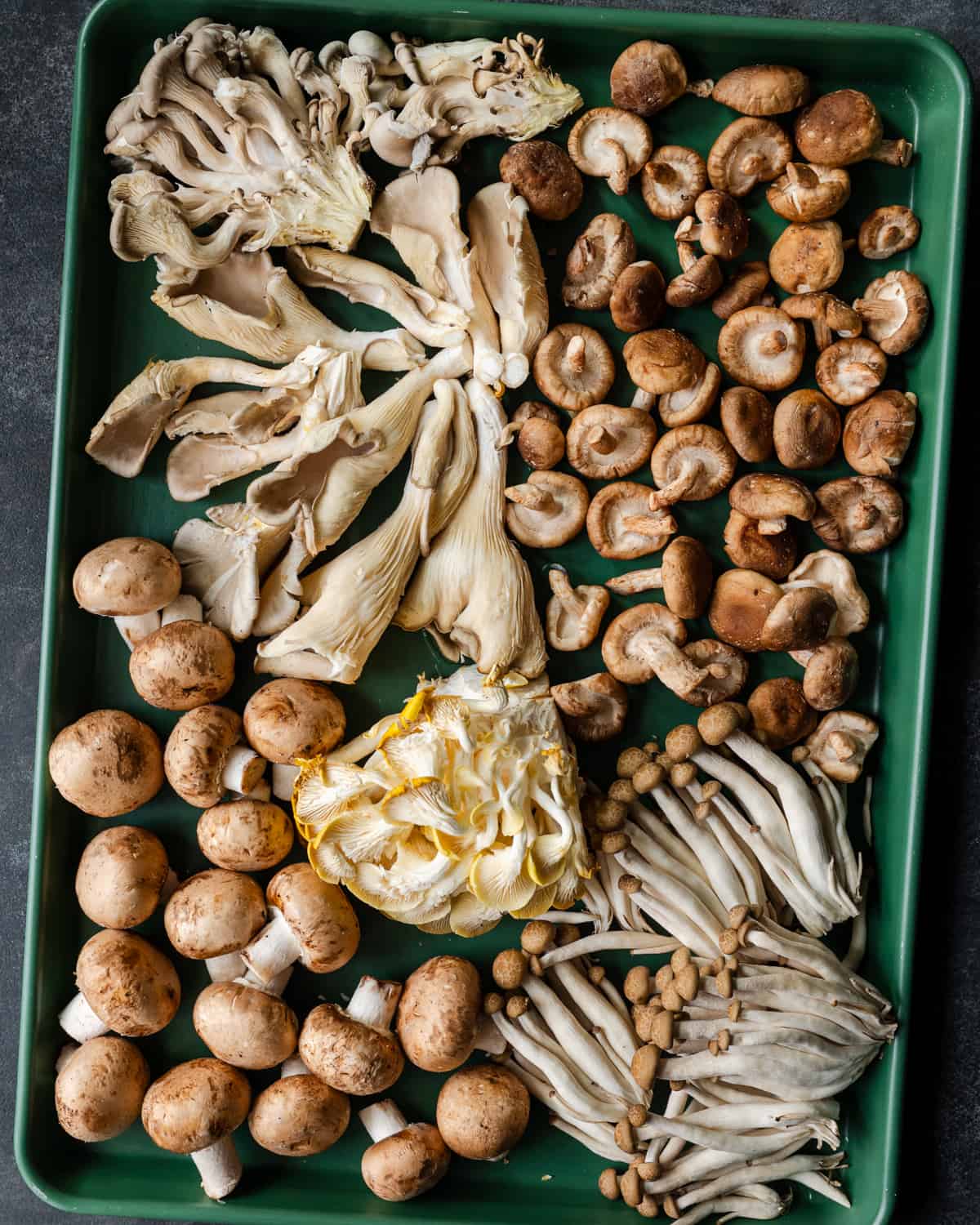 whole raw mushrooms on a green baking sheet.