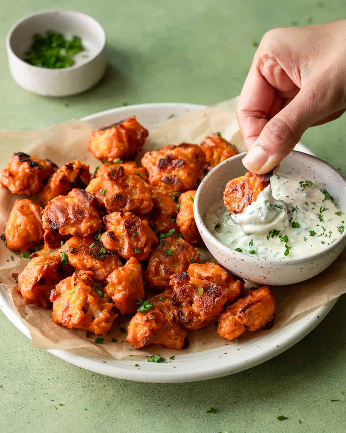 person dipping buffalo cauliflower into ranch in a small bowl.