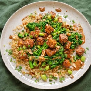 baked peanut tofu with broccolini and edamame on top of brown rice on a ceramic plate.