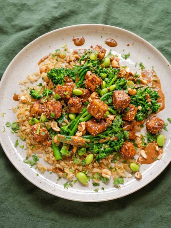 baked peanut tofu with broccolini and edamame on top of brown rice on a ceramic plate.