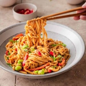 person using chopsticks to pick up sesame noodles from a bowl.